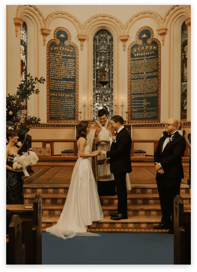 Bride and groom hold hands at the alter in front of Priest